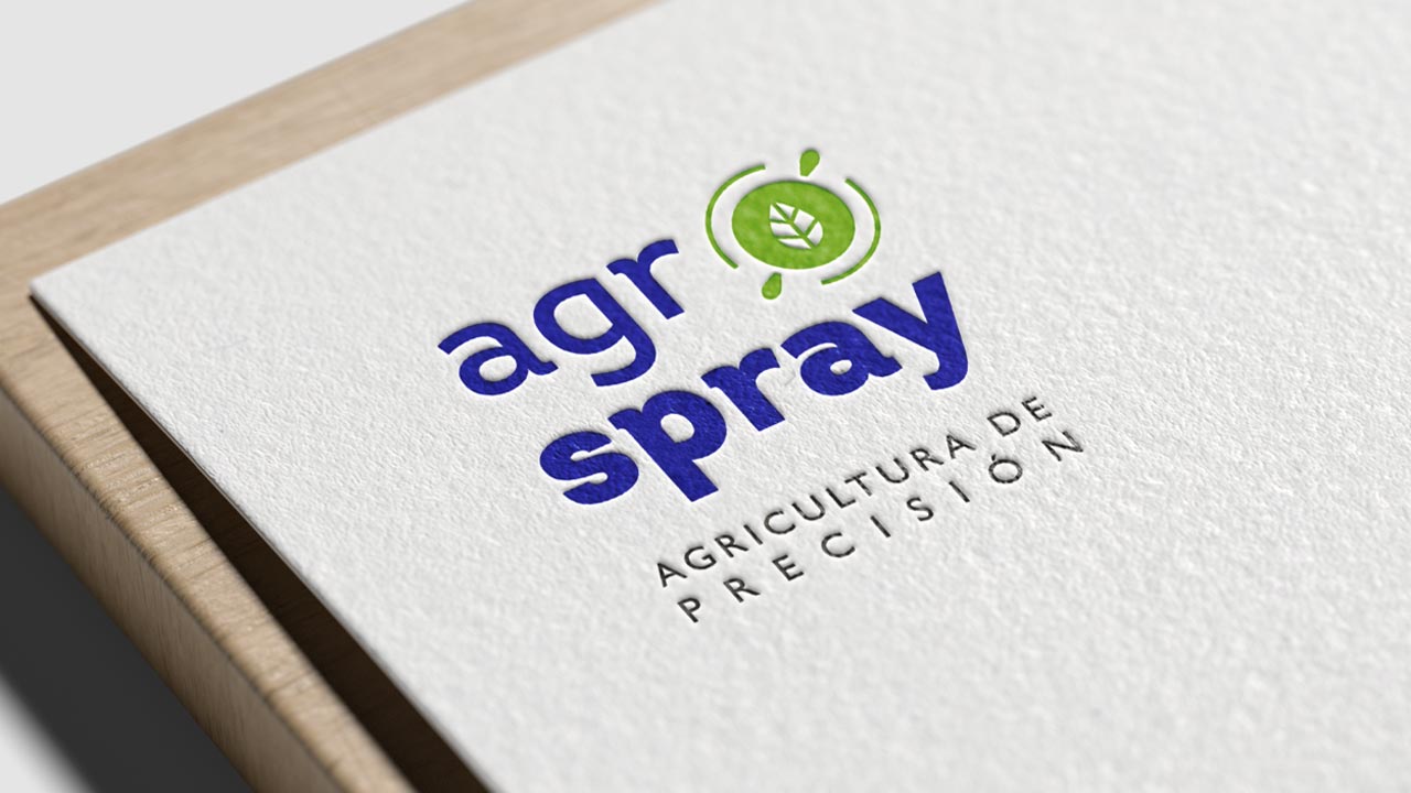 Agrospray-Portafolio-Logotipo-1 Logotipo de AgroSpray en relieve sobre una tarjeta de presentación blanca, con los colores azul y verde predominando. El diseño incluye una hoja dentro de un círculo verde, representando la precisión agrícola. Debajo del nombre, se encuentra el lema 'Agricultura de Precisión' en letras negras.