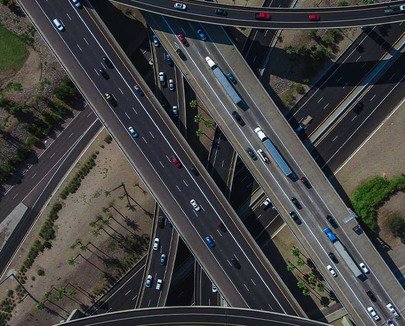 Vista aérea de un intercambio vial con varias autopistas cruzándose, mostrando tráfico fluido de automóviles y camiones en diferentes niveles de la carretera.