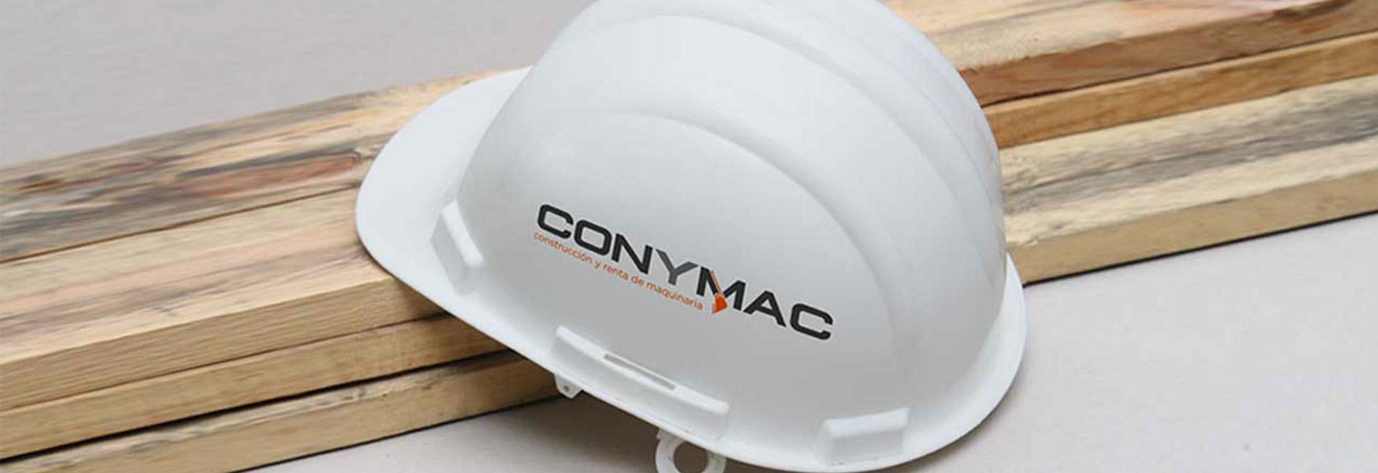 Conymac-Portafolio-Casco Casco blanco de seguridad con el logotipo de CONYMAC, colocado sobre tablones de madera.