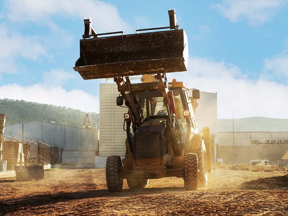 Conymac-Portafolio-Maquinaria-1 Imagen frontal de un tractor amarillo levantando tierra en un sitio de construcción bajo un cielo despejado.