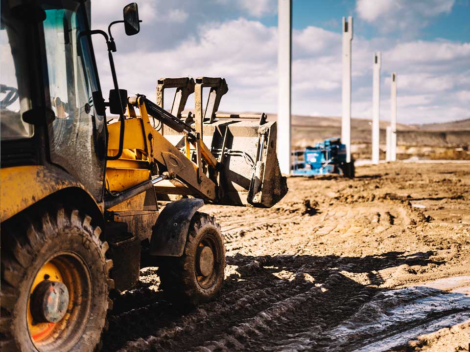 Conymac-Portafolio-Maquinaria-2 Un tractor amarillo trabajando en un sitio de construcción fangoso, con otros equipos de construcción visibles a lo lejos.