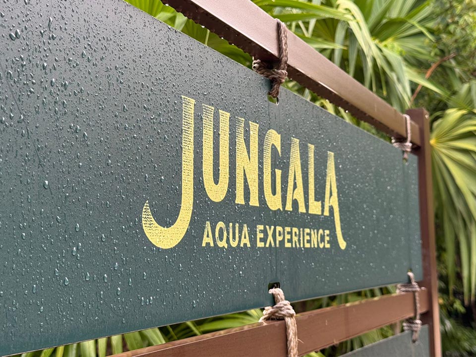 Jungala-Park-Portafolio-Detalle-Reglamento Cartel de bienvenida de Jungala Aqua Experience con diseño en verde y amarillo, mostrando gotas de agua sobre la superficie, montado sobre una estructura de madera.