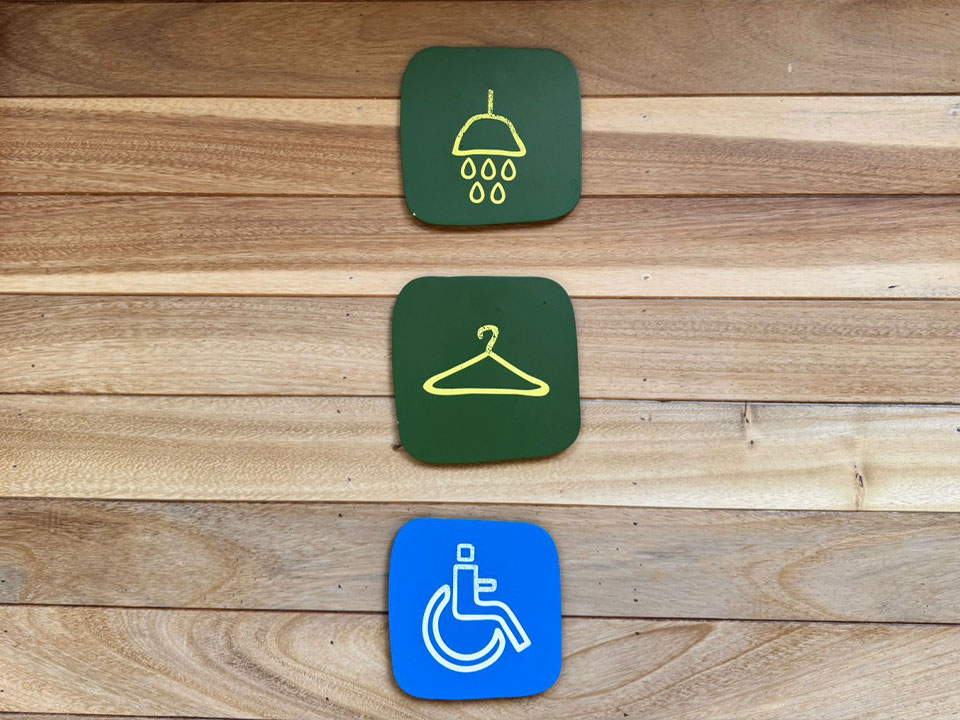 Jungala-Park-Portafolio-Identificativos Señalamientos con tres íconos que representan ducha, vestidor y accesibilidad para discapacitados, sobre una pared de madera en Jungala Aqua Experience.