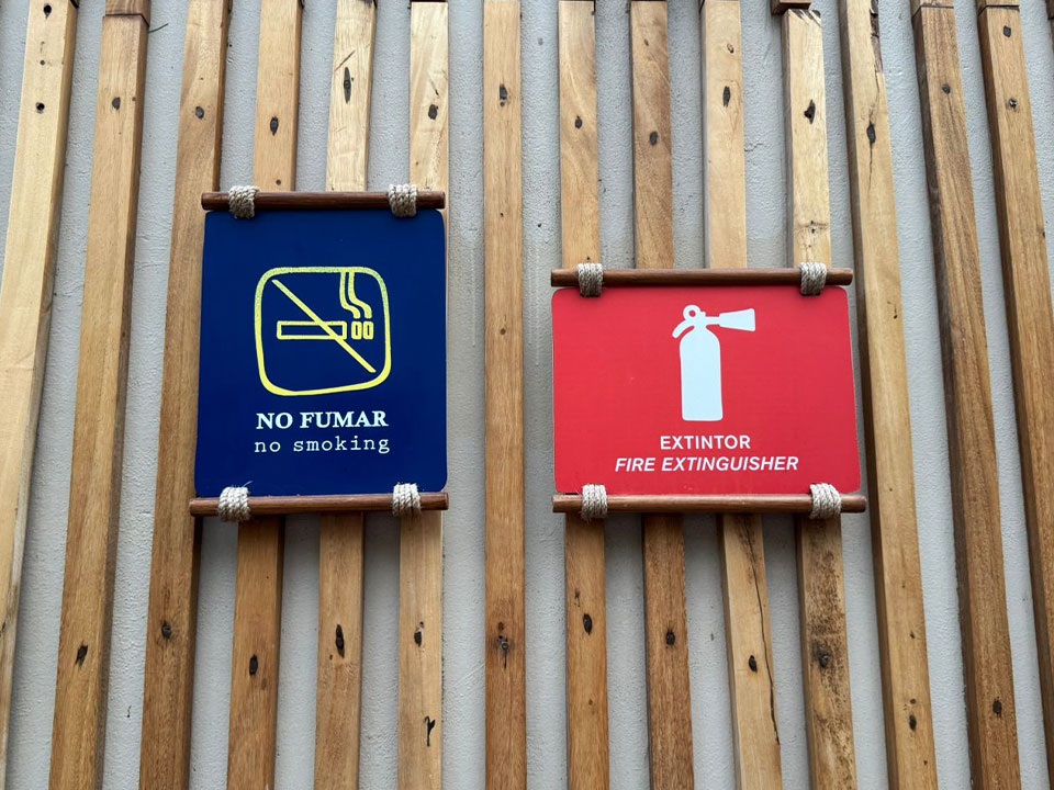 Jungala-Park-Portafolio-Normativos Señalética con un cartel de 'No fumar' y un extintor en Jungala Aqua Experience, con fondo de madera rústica, promoviendo la seguridad del parque.