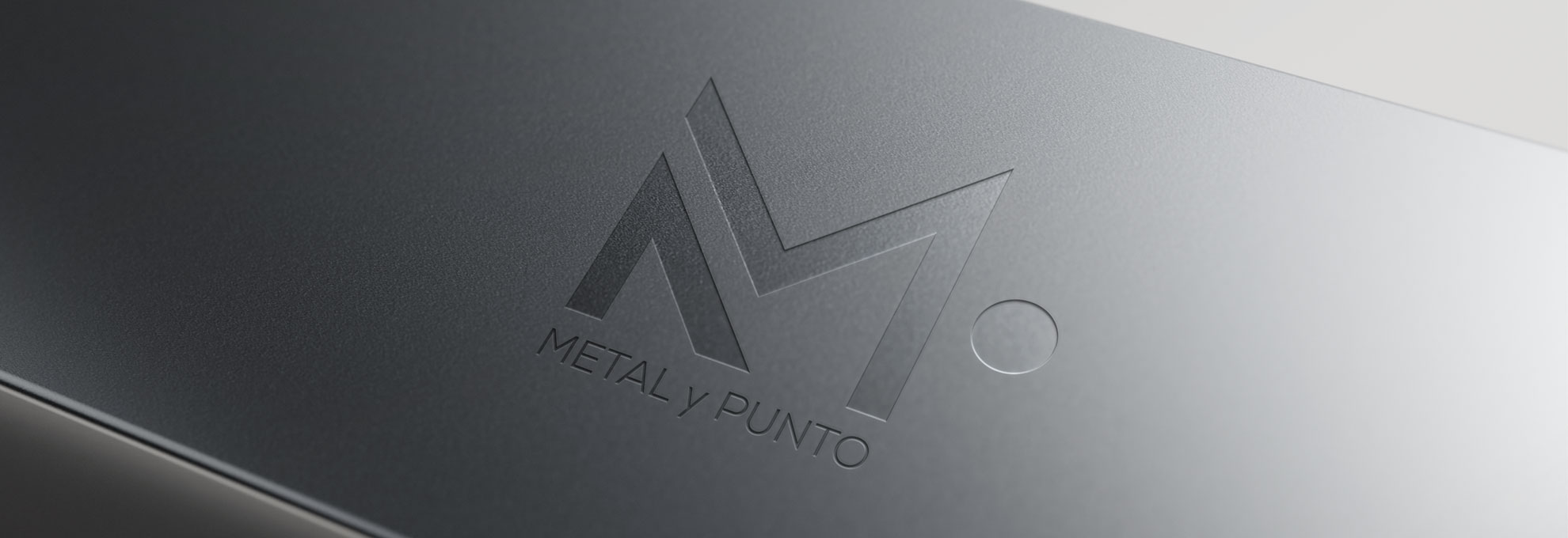 MetalyPunto-Portafolio-Logotipo-1 Logotipo en relieve de la marca Metal y Punto grabado en una placa metálica de acabado oscuro.