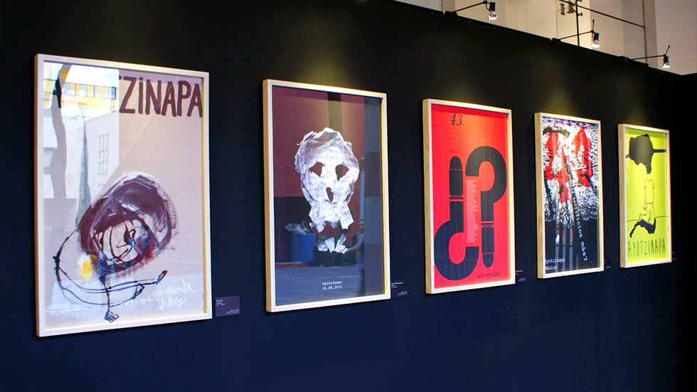 Cinco pósters enmarcados en una exposición de la bienal de carteles de Ayotzinapa, cada uno con un diseño gráfico que explora la tragedia de los estudiantes desaparecidos, utilizando formas abstractas y simbología potente.