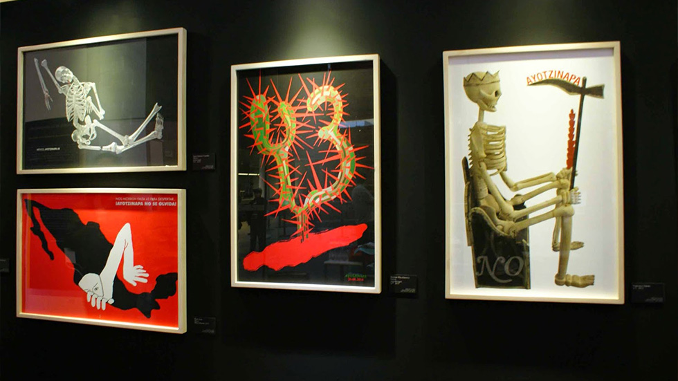 Cuatro obras gráficas enmarcadas en una galería de arte, con esqueletos y símbolos que abordan temas sociales y políticos sobre los estudiantes desaparecidos de Ayotzinapa, como parte de la bienal de carteles de Ayotzinapa.